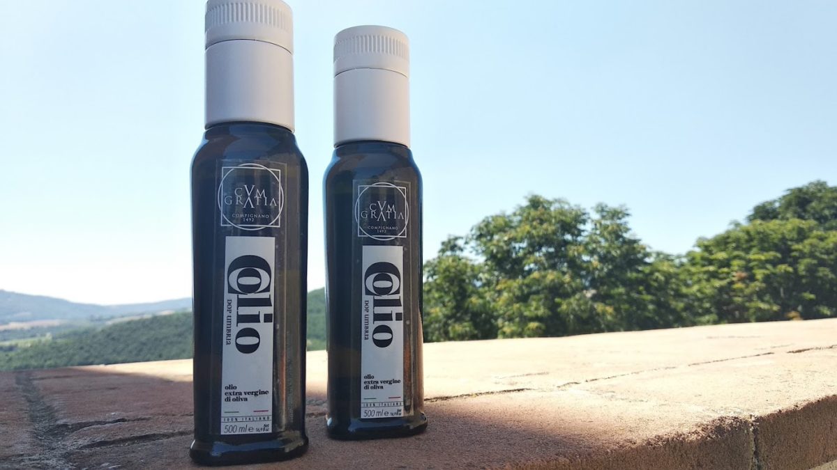 Due bottiglie di COLIO® DOP UMBRIA, con la natura di Compignano sullo sfondo